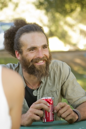 A scruffy young man drinks a beverage and talks to friends.の写真素材