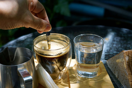 A hand was making with a spoon a hot coffee in a wooden tray on the tables in a cafe then soft sunlight.の写真素材