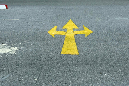 A yellow arrow sign for turn left and right on the asphalt road, concept of direction and directionの写真素材