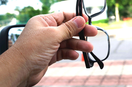 A hand holding a pair of black eyeglasses on blurred background on the car to preparing.の写真素材