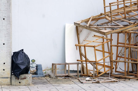 A pile of wooden sticks with a black garbage bag in a construction site beside a cements wall  for texture and backgrounds.の写真素材