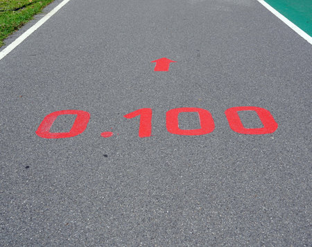 A red distance sign  numbers 0.100 KM  marken on surface the street in the parks