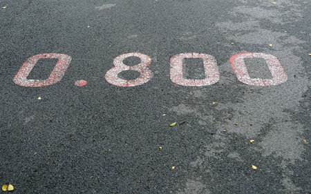 A red distance sign  numbers 0.800 KM  marken on surface the street in the parks