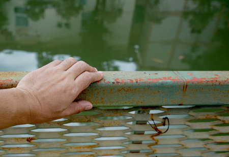 A hand's holding on the old green metal fence with a backside is a water background, lonely concepts.の写真素材