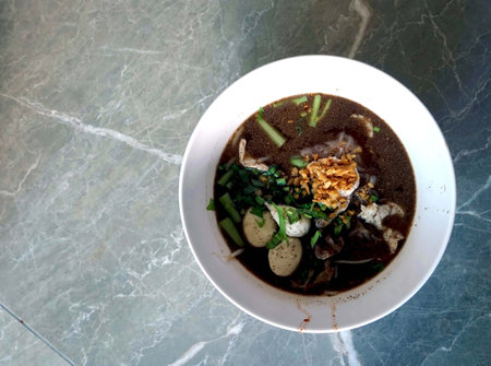 Thai style noodle soup with pork and egg in white bowl