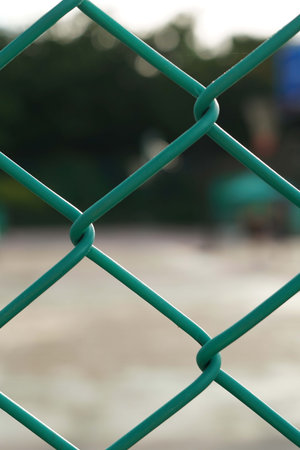 Green chain link fence on the playground. Selective focus with shallow depth of field.