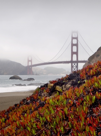 Golden Gate Bridge with Baker Beach and cliffs in foreground and fog covering up part of the towersの写真素材