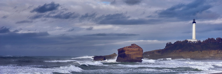 Lighthouse of Biarritz under a dark sky with clouds and a rough seaの写真素材