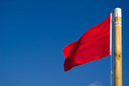 Red flag closeup in a beach. Red flag is a sign of warning and means that it's not advisable to take...