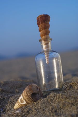 Summer composition with a glass bottle and beautiful shell at sunset