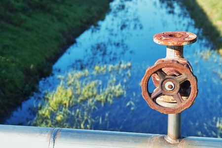 water valve wheel with an irrigation channel in the backgroundの写真素材