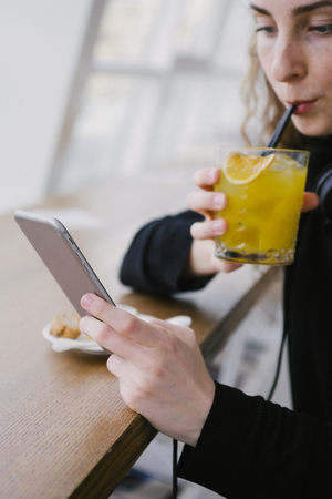 Young trendy woman holding an orange cocktail and listening to musicの写真素材