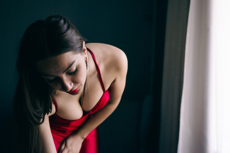 Sexy gorgeous beautiful girl standing in  room near mirror with red dress, elegant hair-style and make-upの写真素材