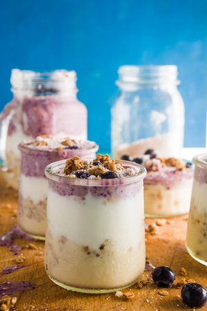 Frontal view of a delicious breakfast yogurt parfait made with fresh yogurt, strawbery smothie and ananas smoothie with granola layer and blueberry as decoration on a rusty blue  wooden tableの写真素材