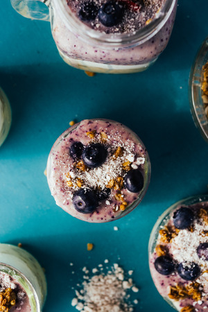 Top view of a delicious breakfast yogurt parfait made with fresh yogurt, strawbery smothie and ananas smoothie with granola layer and blueberry as decoration on a rusty blue tint green wooden tableの写真素材