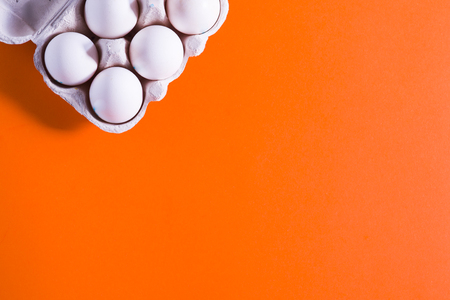 Six naturally white hens eggs in a white paper carton on orange background, top view, copyspace provided to add textの写真素材