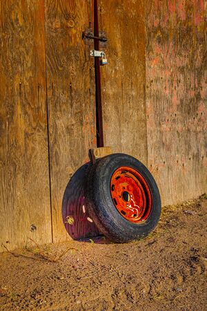 A well-used red-rimmed tire sits agaiinst a shed door as the sun casts an interesting shadow on the woodの写真素材