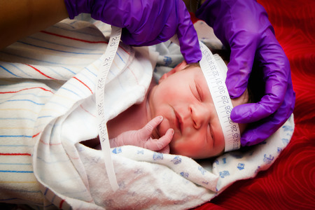 The purple gloves of a midwife measure the head width of a newborn infant after he was born at home.