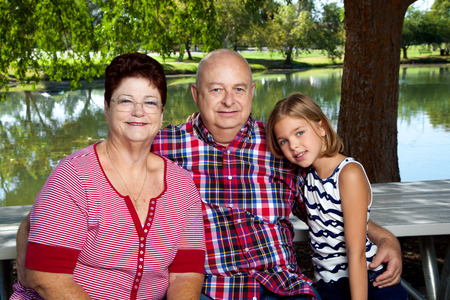 A young girl sits at a picnic table in the park with her grandparents.  They are wearing red, white, and blue.  The picnic table is in front of a bond.の写真素材