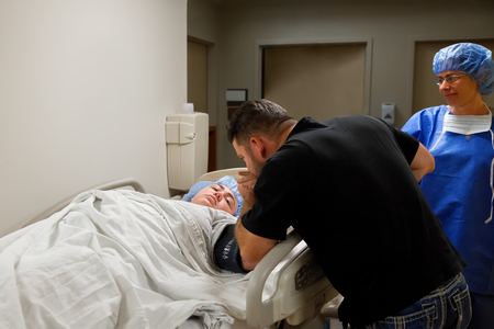 A father kisses his daughter's hand as she is being taken back for an emergency C-Section.の写真素材