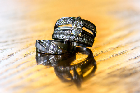 A brideâ??s wedding ring sits atop the ring of her groom.  They are both on yellow wood.