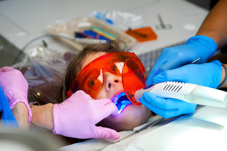 A scared looking little girl looks at her dentist with wide eyes as she has an LED light curing new seals on her teeth.の写真素材