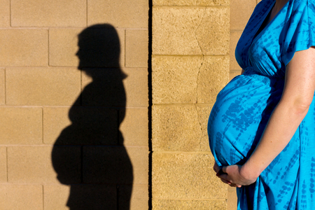 A pregnant woman takes a walk during early stages of labor.  Her shadow is cast on a neighborhood wall.  Lots of copy space.の写真素材