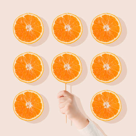Pattern made of orange fruit slices on bright beige  background with Child's hand holding a stick...