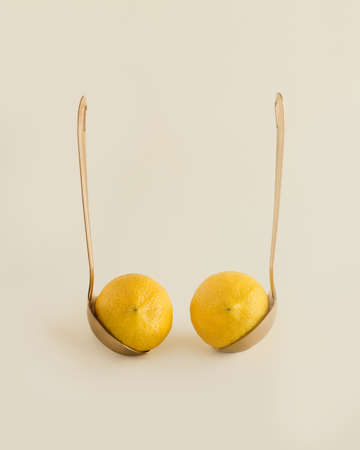 Provocative arrangement with couple of lemons in gold luxurious ladles, isolated on pastel beige...