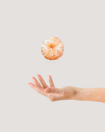 Beautiful young womanâs hand juggling juicy, peeled tangerine. Organic, raw, healthy food concept. Citrus fruit minimal arrangement isolated on pastel beige background.の写真素材