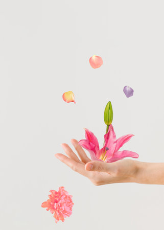 Creative floral poster with beautiful young womanâs hand which holds pink lily blossom isolated on pastel beige background. Summer festive and celebration concept. Invitation and greeting card idea.の写真素材