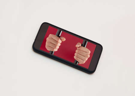 Male hands try to break prison bars on the screen of the cell phone isolated on beige background. Minimal, abstract, conceptual scene. Liberation from addiction of mobile phones or social networks.の写真素材