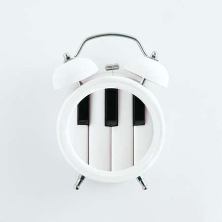 White alarm clock with piano keys isolated on pastel white background. Fun, aesthetic, abstract layout. Time for playing classic music, piano party or music school creative idea. Minimalistic concept.の写真素材