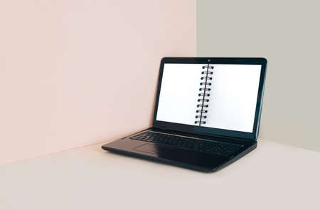 Minimal office workspace made of laptop and white opened notepad. Online education, remote work or distance learning concept. Abstract scene with copy space isolated on pale pastel beige background.の写真素材