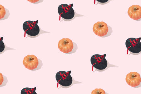 Minimal festive halloween pattern made of black witch hats with red ribbons and orange pumpkins isolated on pastel pink background. Halloween party or celebration invitation card concept.の写真素材