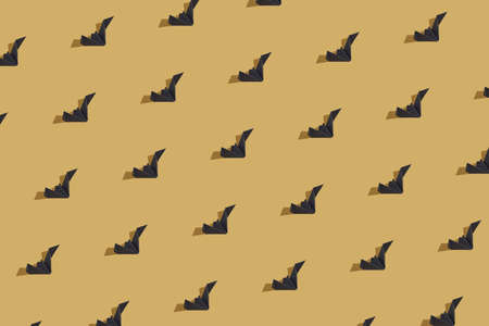 Halloween texture made of black paper origami bat isolated on gold background. Sun and shadows....