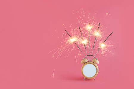2022. Minimal abstract Christmas festive scene with alarm clock and sparklers isolated on pastel pink background. Celebration, anniversary or birthday concept. Party Invitation card idea.の写真素材