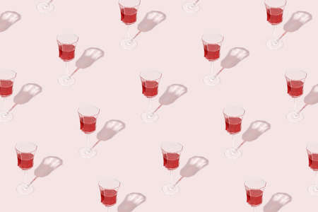 Minimal pattern made of wine glasses with red wine isolated on pastel pink background. Drink for party, wine shop or wine tasting concept. Sun, shadows and reflections. Summer Mediterranean texture.の写真素材