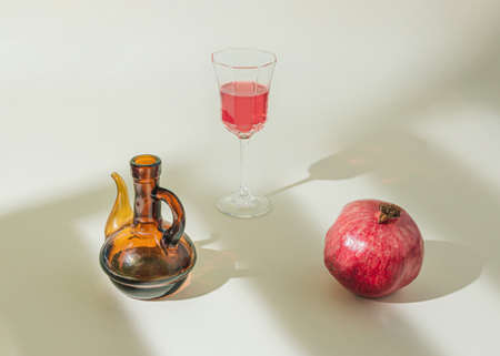 Minimal fruit and beverage scene with pomegranate, bottle and wine glass with red wine or juice isolated on the pastel beige background. Sun and shadows. Raw natural healthy food and drink concept.の写真素材