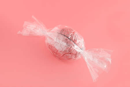 2022. Minimal satiric scene made of human brain model wrapped in cellophane isolated on pastel...