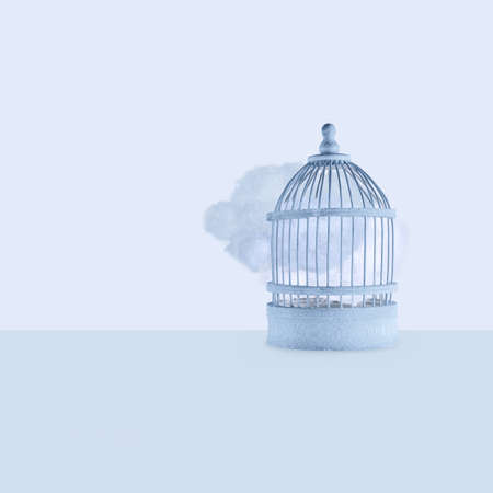 Dark clouds are released from closed bird cage and float in space on pastel blue background. Minimal creative concept of bad ideas to prevent environmental pollution or trapped and unfulfilled dreams.の写真素材