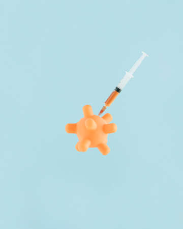 2022. Orange model of coronavirus received vaccine. Minimal abstract card with pastel blue isolated background. Concept of immunization, vaccination or prevention of covid-19. Idea of ending pandemic.の写真素材