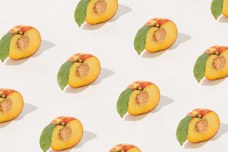 Minimal summer fruit pattern made of halved peaches with stones and leaves on isolated pastel beige...