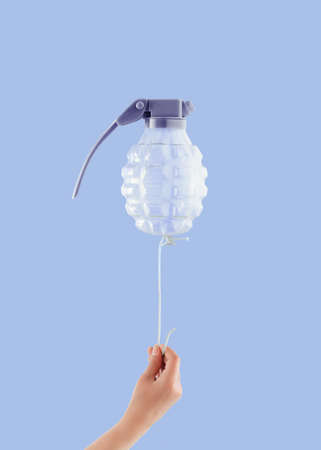 Childâs hand holds a rope with a tied balloon in the shape of a bomb on isolated pastel purple background. Minimal creative abstract dystopian concept. Anti-war idea. Danger of childrenâs war games.の写真素材