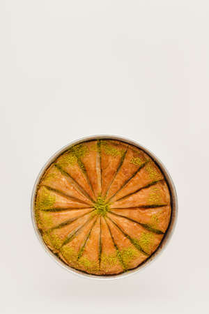 Sweet pastry - baklava cut into slices, stands in a round tray on an isolated pastel beige background with copy space. Note card for traditional baked dessert. Minimal concept of delicious food.の写真素材
