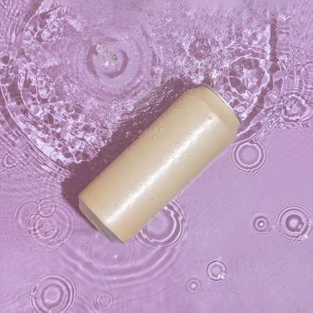 Beige can with refreshing drink floats in pastel purple-pink water. Reflections of sun and shadows....