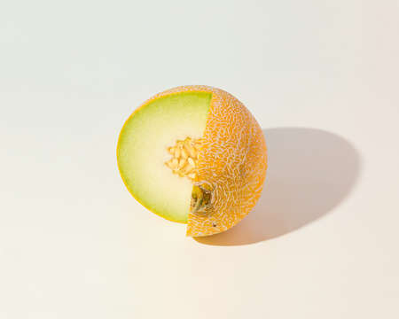 Minimal summer fruit scene made of cut sunlit melon on isolated pastel beige background. Sun and...