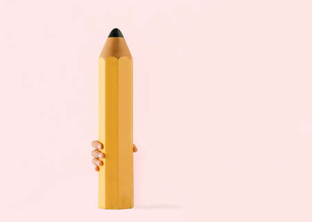 Child's hand holds huge pencil on isolated pastel pink background. Drawing or writing. Back to school. Minimal concept of education. The idea of difficult school exercises.の写真素材