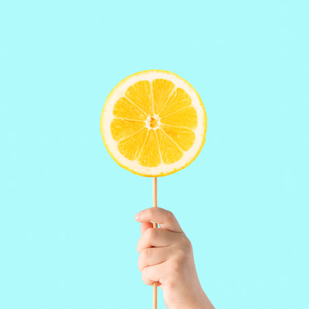 Healthy sweets concept made with childâs hand holding stick with a lemon slice, against vibrant turquoise blue background. Minimal creative food scene. The idea of citrus lollipop.の写真素材