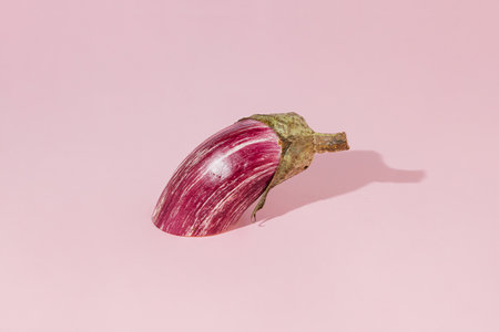 Halved purple eggplant on pastel pink background. Minimal abstract autumn vegetable concept. Sun and shadows. The idea of raw healthy natural food or organic agricultural products.の写真素材